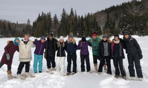 A group of students in winter gear and snowshoes stand smiling with their arms around each other.
