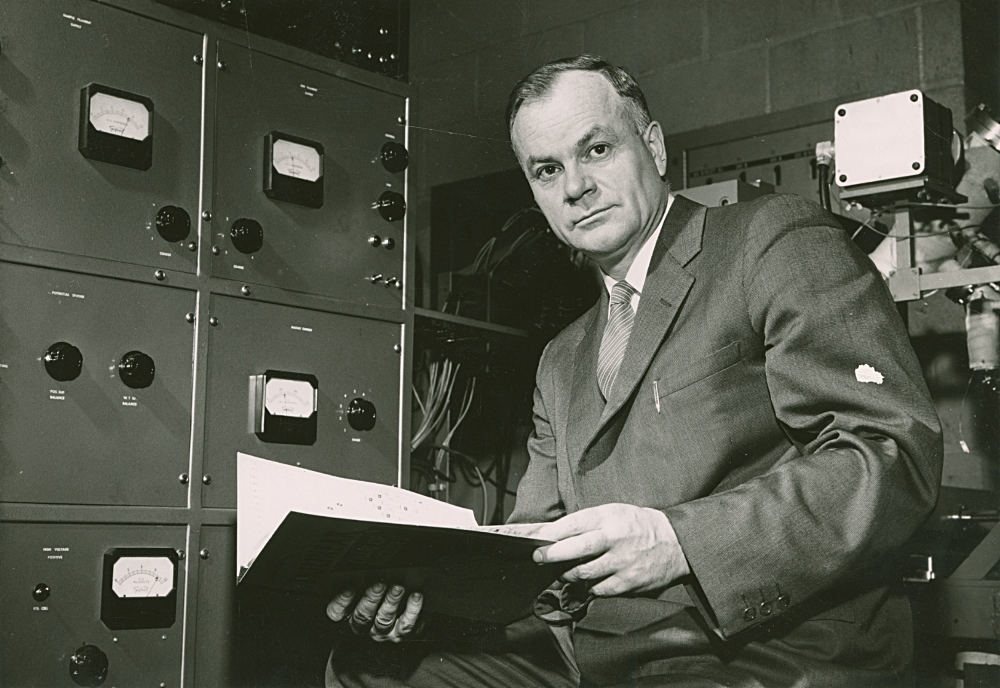 Image of Henry Those reading files in front of a filing cabinet circa 1960.