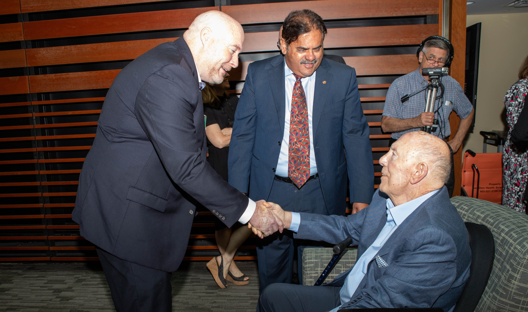 Corporal John Brown, shakes Michael G. DeGroote's hand at the funding announcement, watched by Ramesh Zacharias.