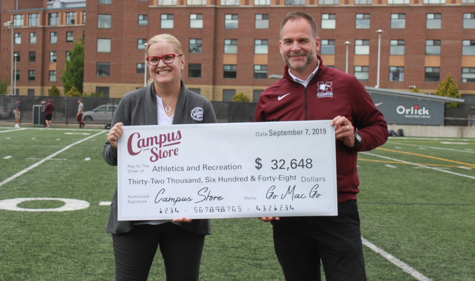 Donna Shapiro and Shawn Burt hold a large display cheque for $32,648 while standing on the football field