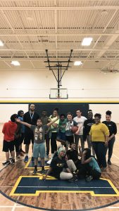 A group of elementary, high school and university students stand on a basketball court