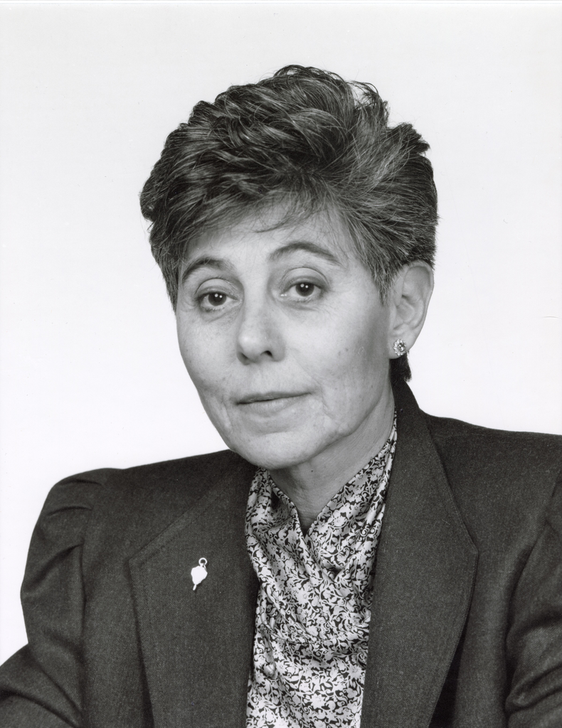 A black-and-white photo of May Cohen. She is wearing a blouse and blazer and is looking at the camera without smiling. 