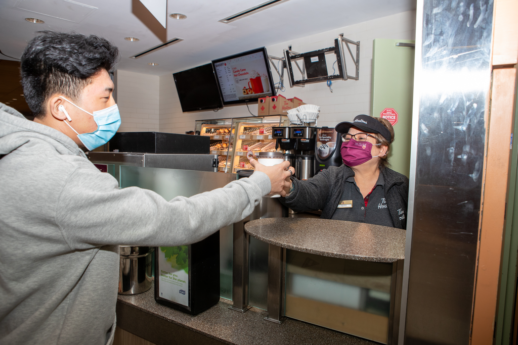 A photo of Terri, a Tim Hortons worker, handing a coffee to a McMaster student