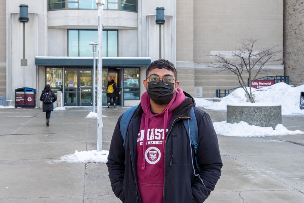 A masked McMaster student standing outdoors on McMaster's campus