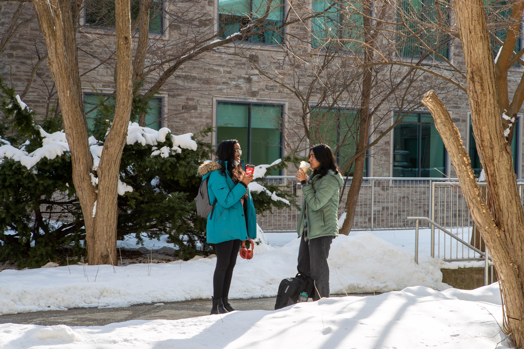 Two female students stand drinking coffee on McMaster's campus 