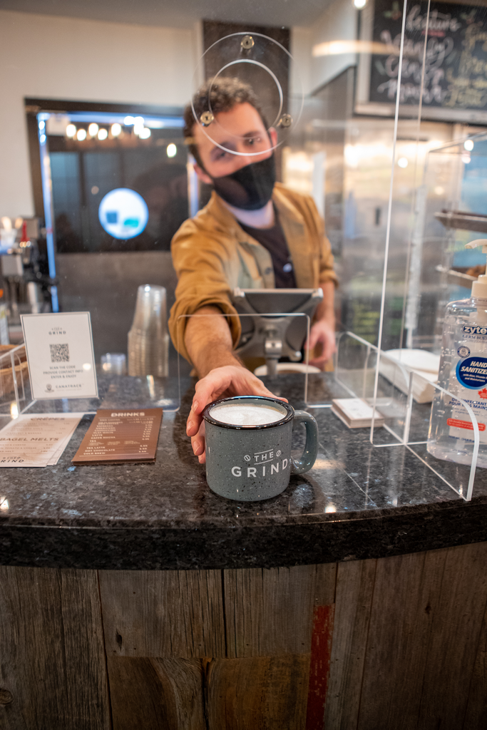 A McMaster Grind employee serves up a mug of coffee through a plexiglass plate 