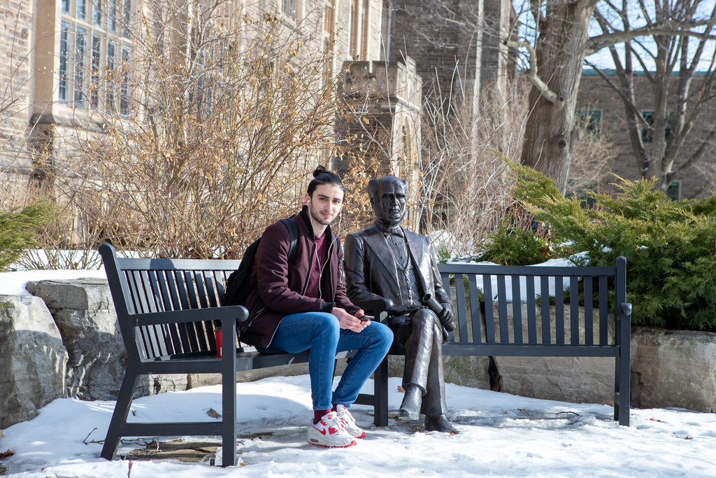 A McMaster students sits beside the Senator William McMaster Statue 