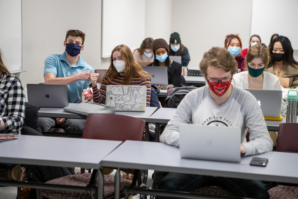 A group of McMaster students inside a classroom. Two of the students are looking at the camera and fit bumping. 