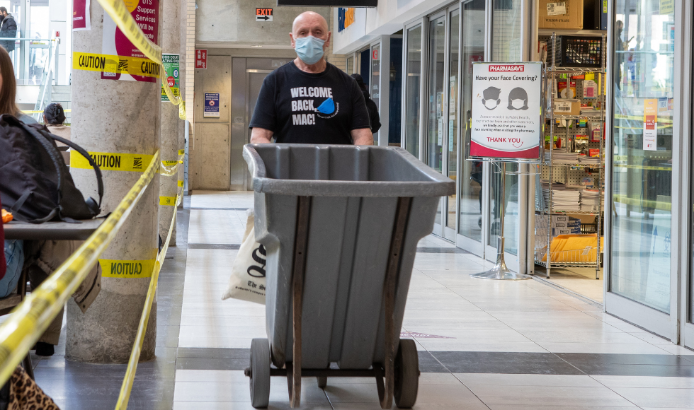 A photo of a McMaster University Student Centre employee pushing a cart. He is wearing a t-shirt that reads 'Welcome back students."