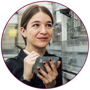 Lianne Grieves in the lab, working with birds holding a pen and notebook