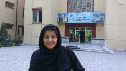 A photo of Marufa Shinwair standing outside Kabul University and smiling at the camera.