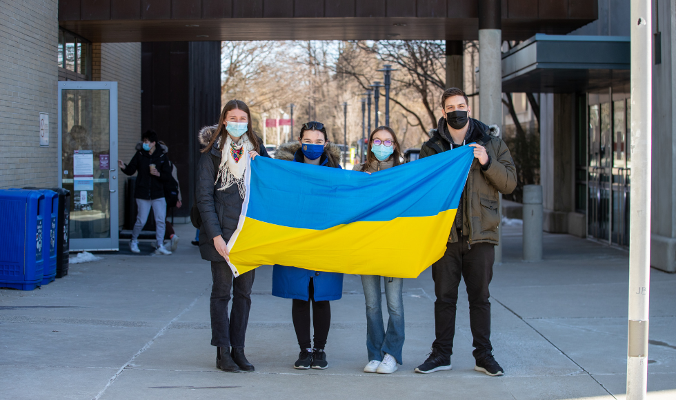 four masked students hold a Ukrainian flag outside a student centre.