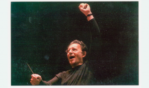 Boris Brott with his arm stretched over his head as he conducts an out-of-view orchestra