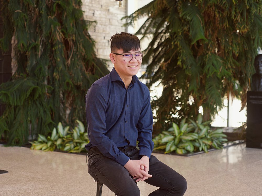 Jayco Cheng sitting on a chair with greenery behind him 