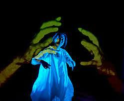 A person performing on stage while a pair of green hands are projected onto a screen behind them
