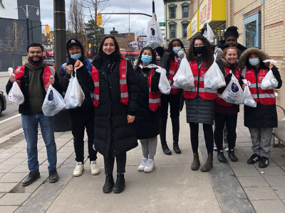 A group of McMaster students holding food packages on a downtown sidewalk
