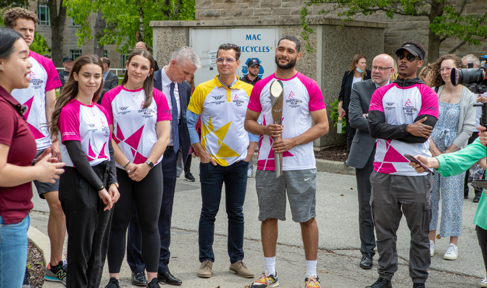 Researcher speaks to group wearing relay shirts about the Nuclear Reactor, outside of the Nuclear Reactor Building on McMaster campus