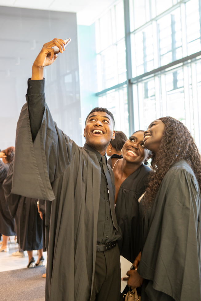 3 smiling students take a selfie in their graduation gowns