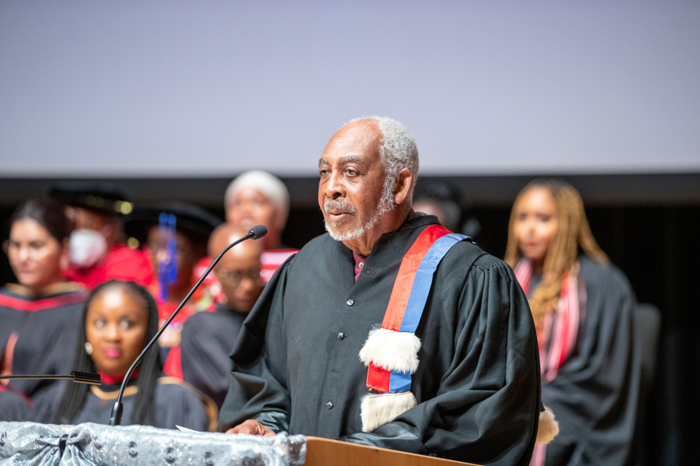 Professor Gary Warner in a convocation gown speaks at the podium.