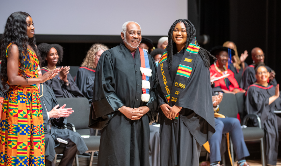 Gary Warner and a student, both in academic gowns, smile on the stage.