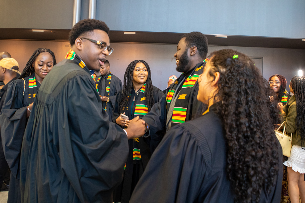 A group of smiling students proudly wearing their graduation gowns and Kente stoles.