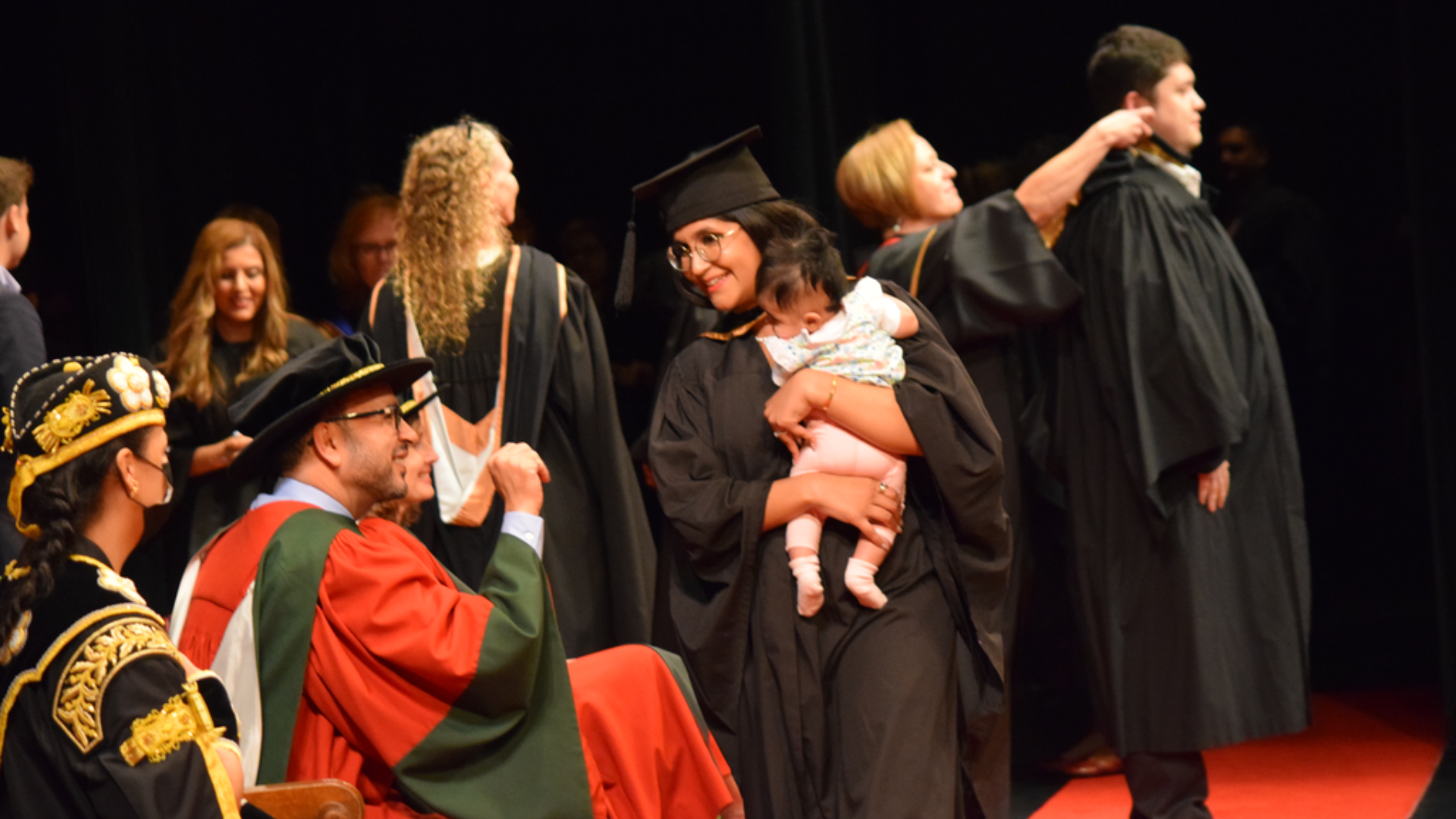 A DeGroote School of Business graduate crosses the stage at convocation with her baby in her arms 