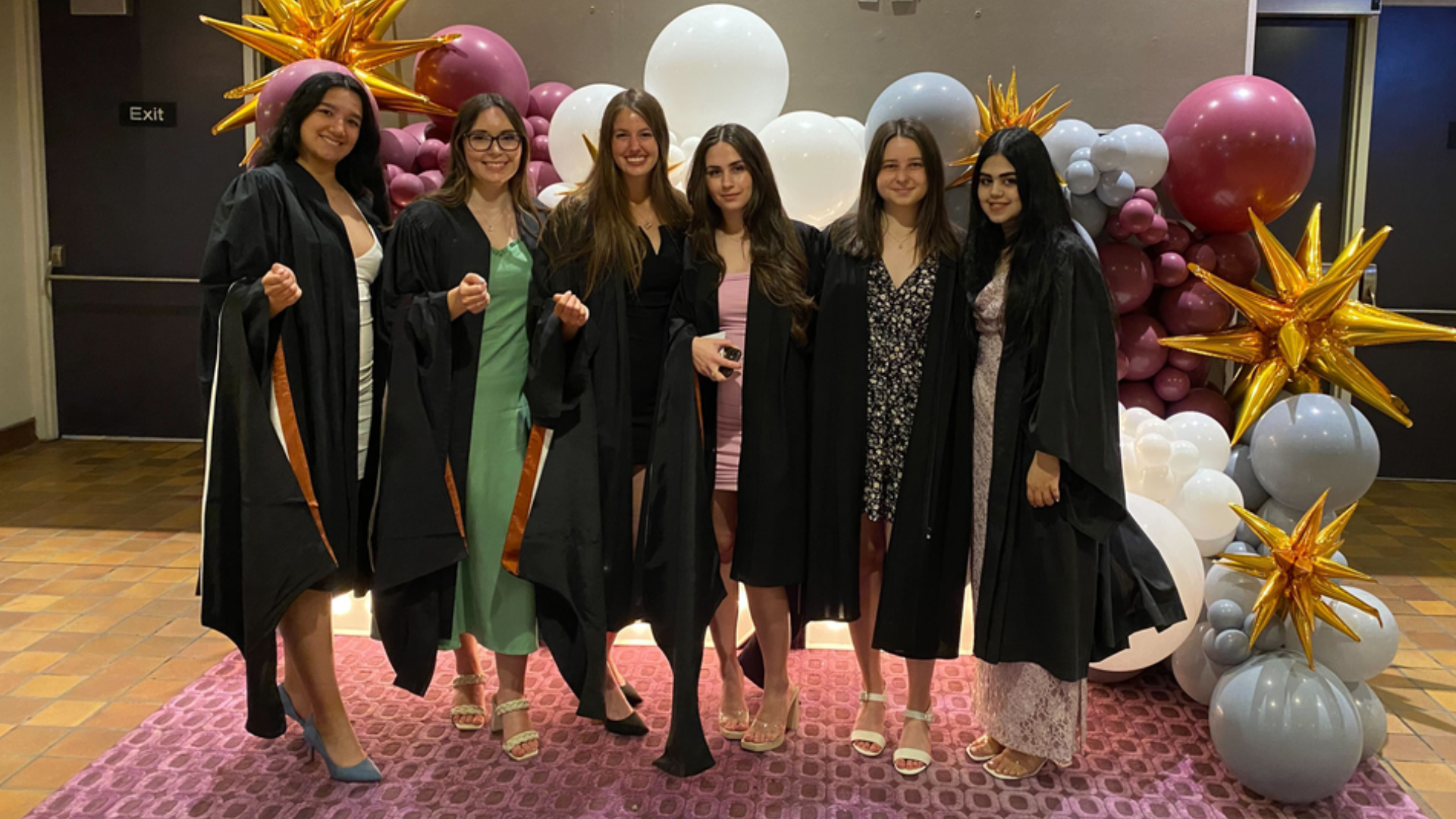 A group of graduates with their convocation hoods on their arms pose for a photo