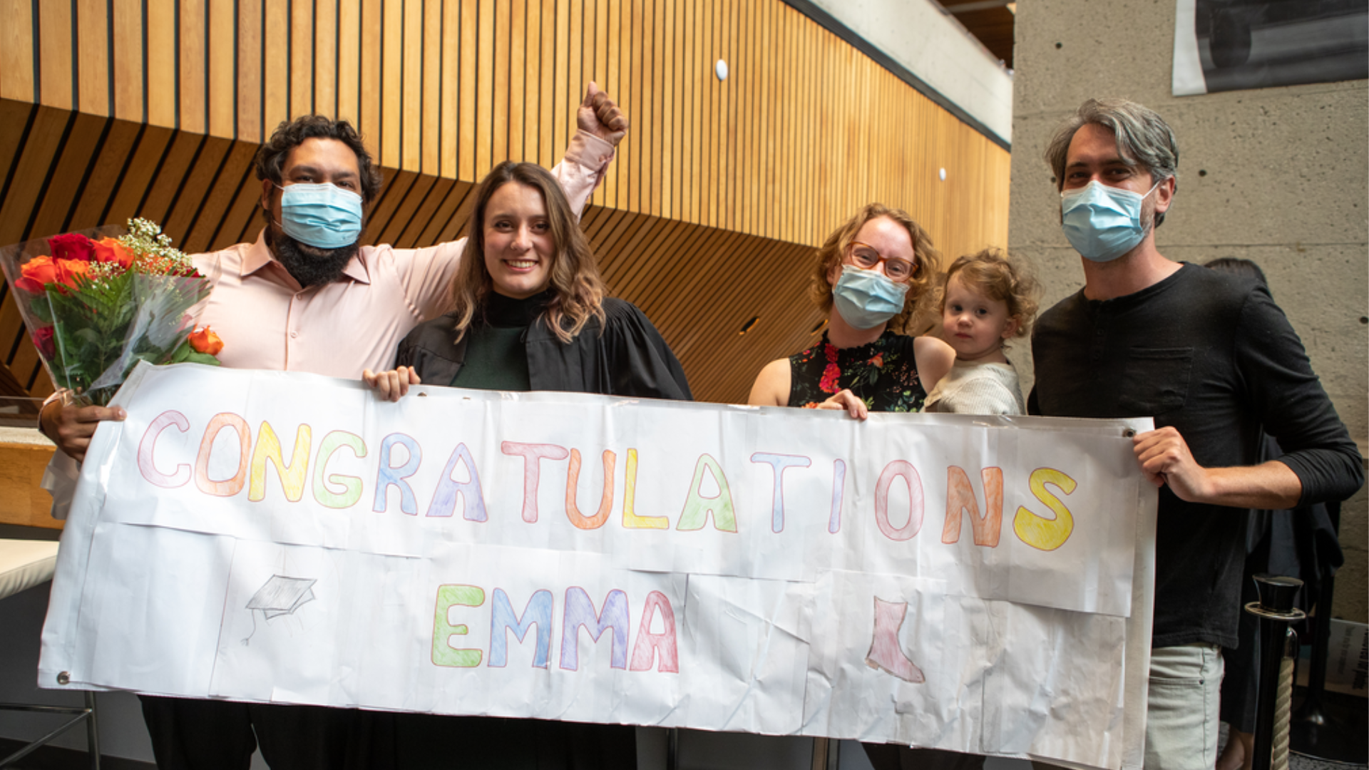Midwifery grad Emma Witkowski and her family posing with a banner that reads 'congratulations Emma'