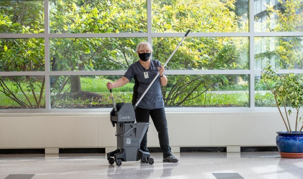 Mirjana holding a mop on a very shiny floor, in front of a window