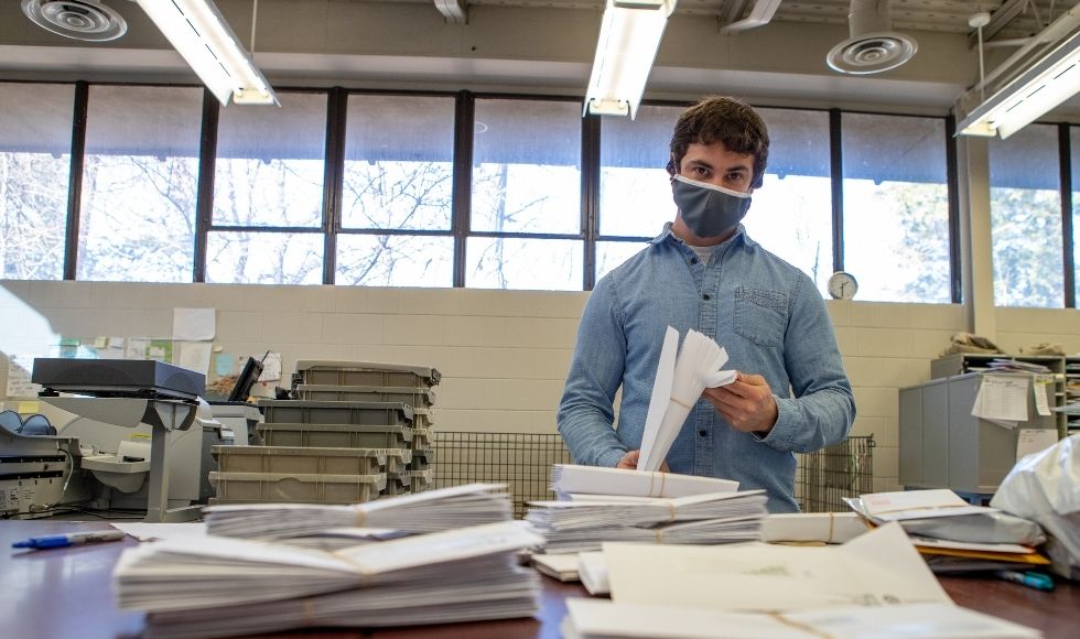 Nick, wearing a mask, at a counter covered in mail and papers