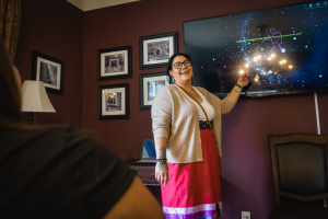 IUSRS participant Bonita Bohnet standing in front of and pointing at a screen that has a star system on it. 