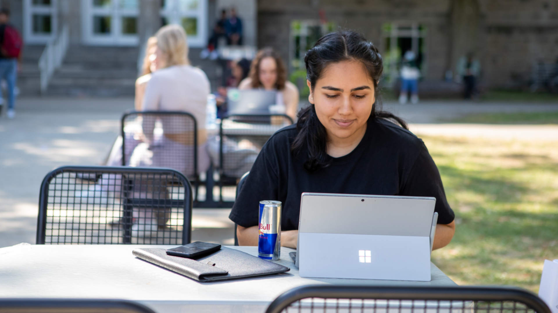 A student seated outdoors looking at their open laptop