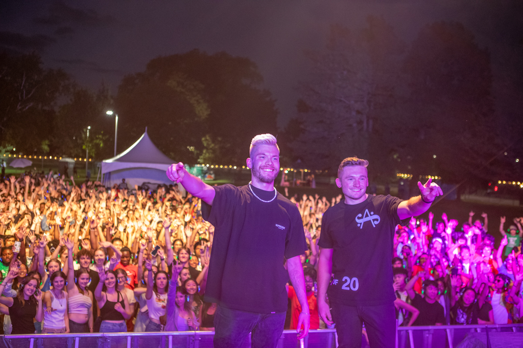 Two performers standing on stage with their backs to a crowd of students with their hands raised