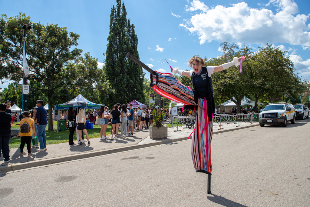 A circus performer in stilts with one leg raised up high and their arms outstretched