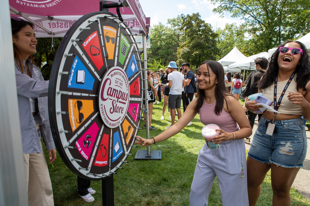 A student turns a wheel to win a prize as another looks on laughing