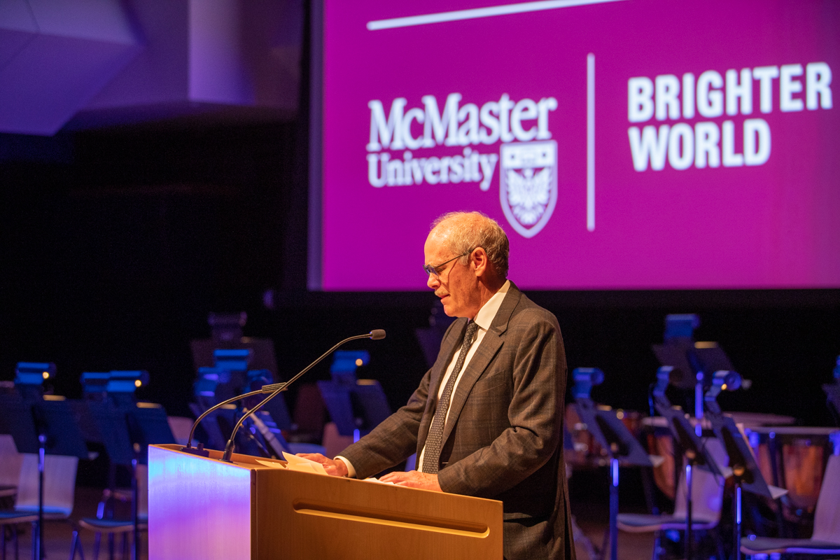 David Farrar standing at a podium. Behind him is a screen with the McMaster University logo on it. 