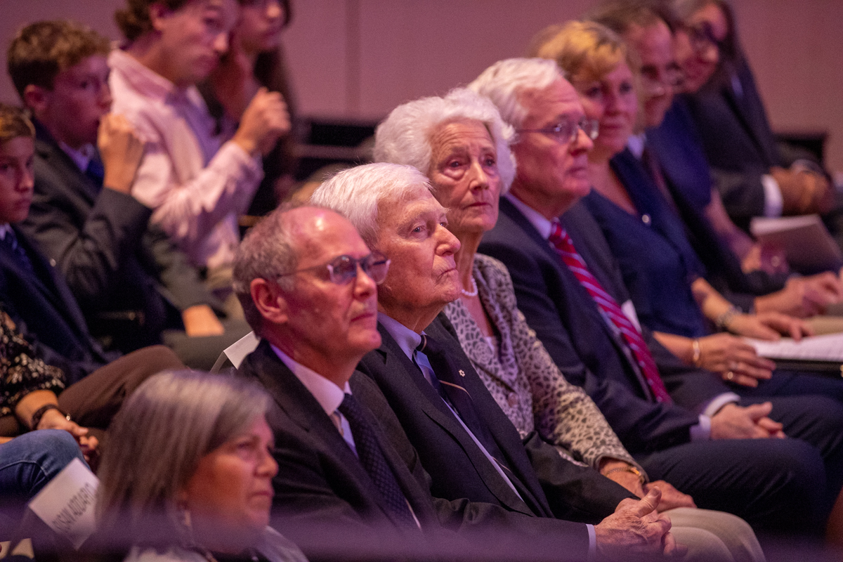 A crowd of people including David Farrar, Lynton Wilson and his wife sit listening as someone delivers a speech. 