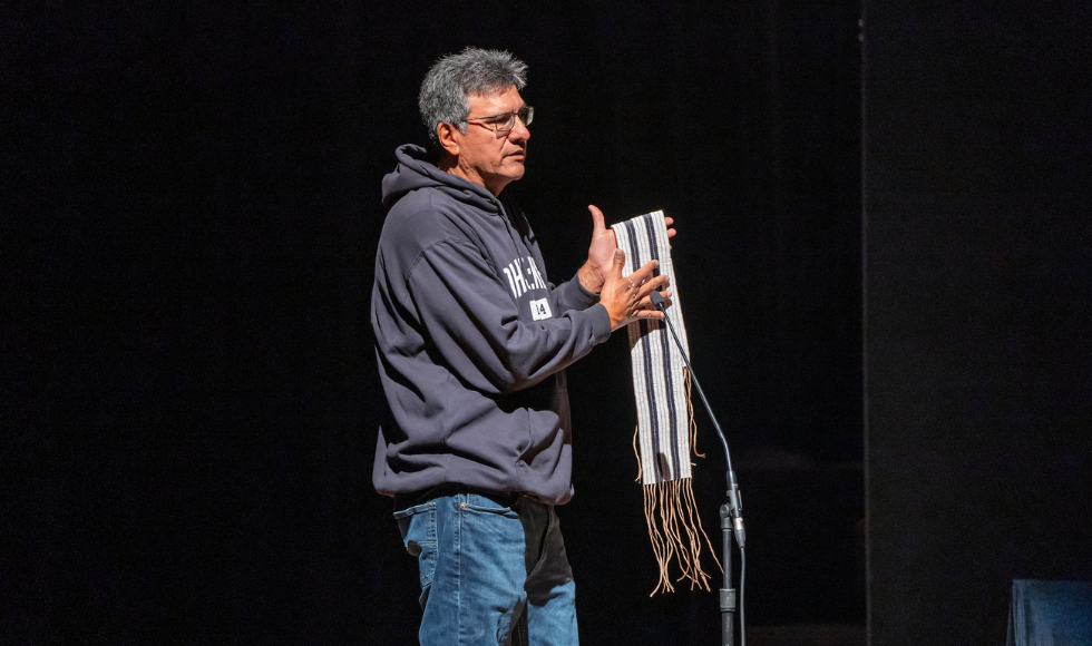 A man stands on stage holds a wampum