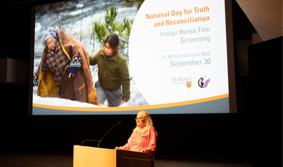 Kathy Knott at a podium in front of a screen with a graphic that shows an image from Indian Horse.