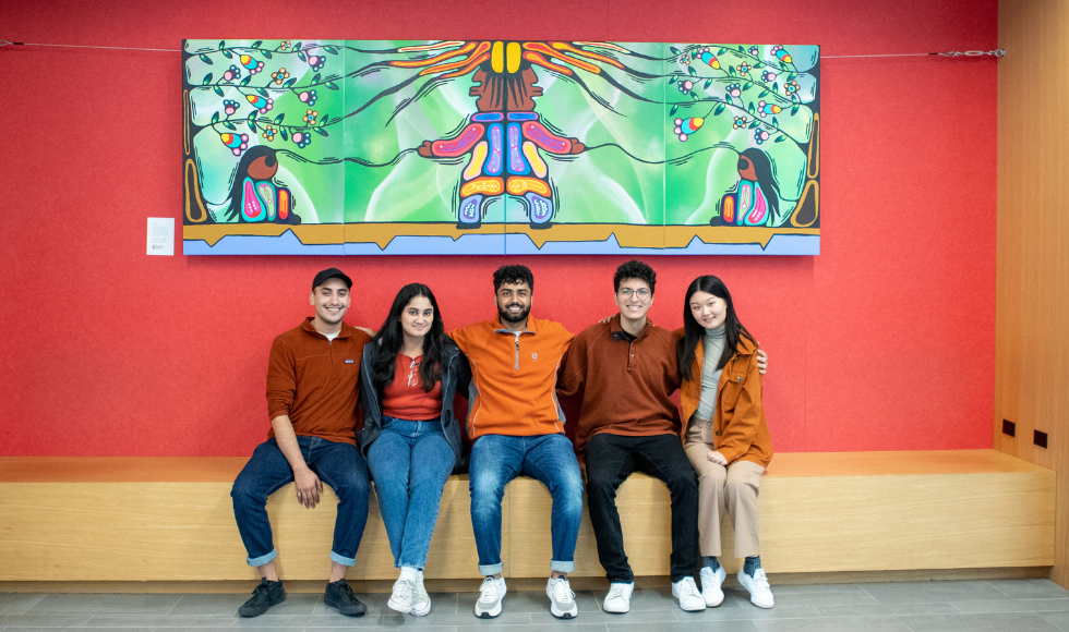 5 students sit under a newly installed mural in PGCLL.