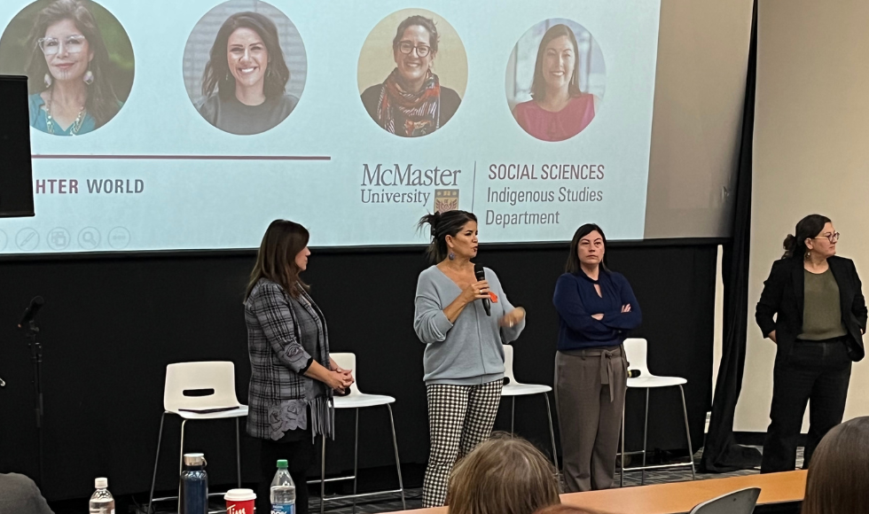 Four speakers on stage against a backdrop of a slide showing their images.