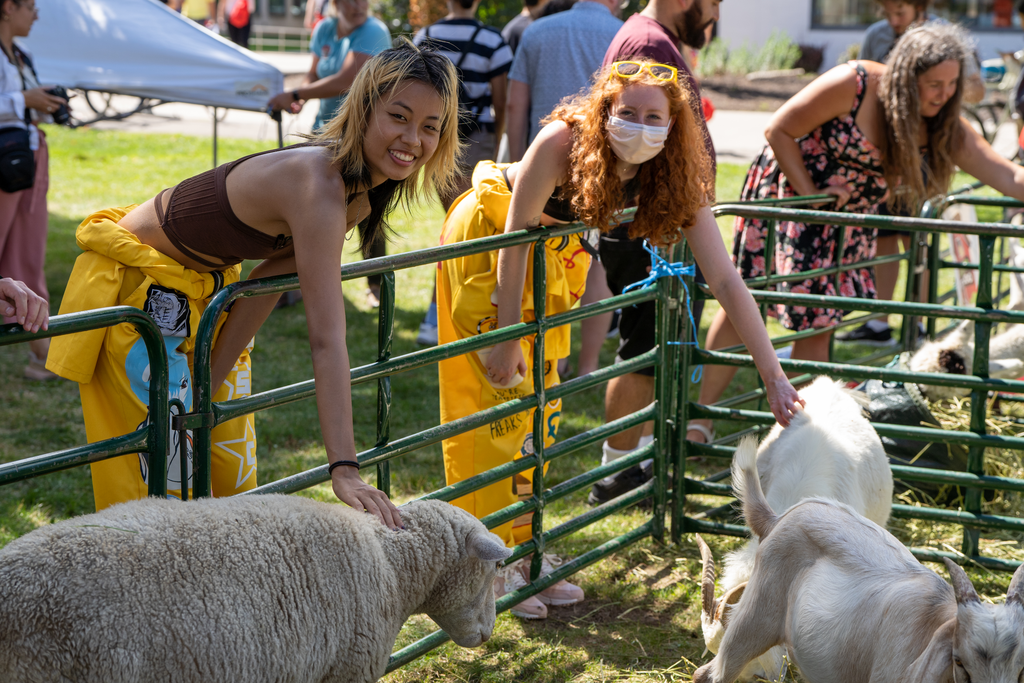 Two students smiling at the camera as they pet farm animals