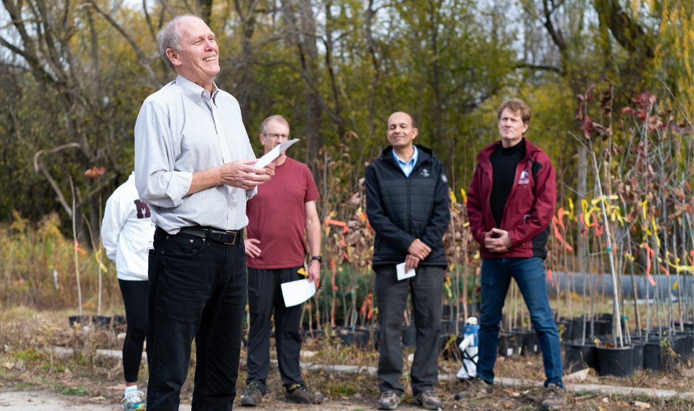 David Farrar laughing in the foreground, outdoors. Behind him are some faculty members, also smiling.
