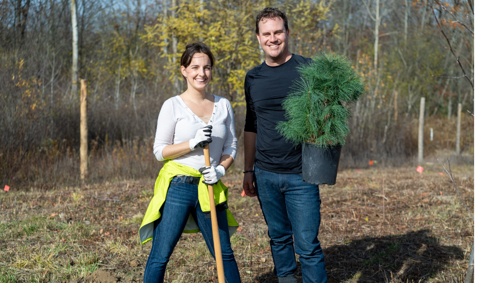 Lejla Latifovic holding a shovel standing beside a man holding a young pine sapling.