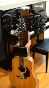 An acoustic guitar sits in a stand with mechanical tuning pegs.  There is a logo 