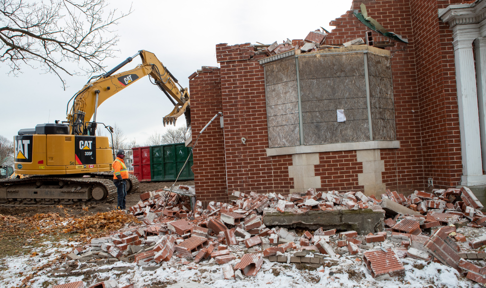 A large piece of heavy machinery beside a partially demolished home.