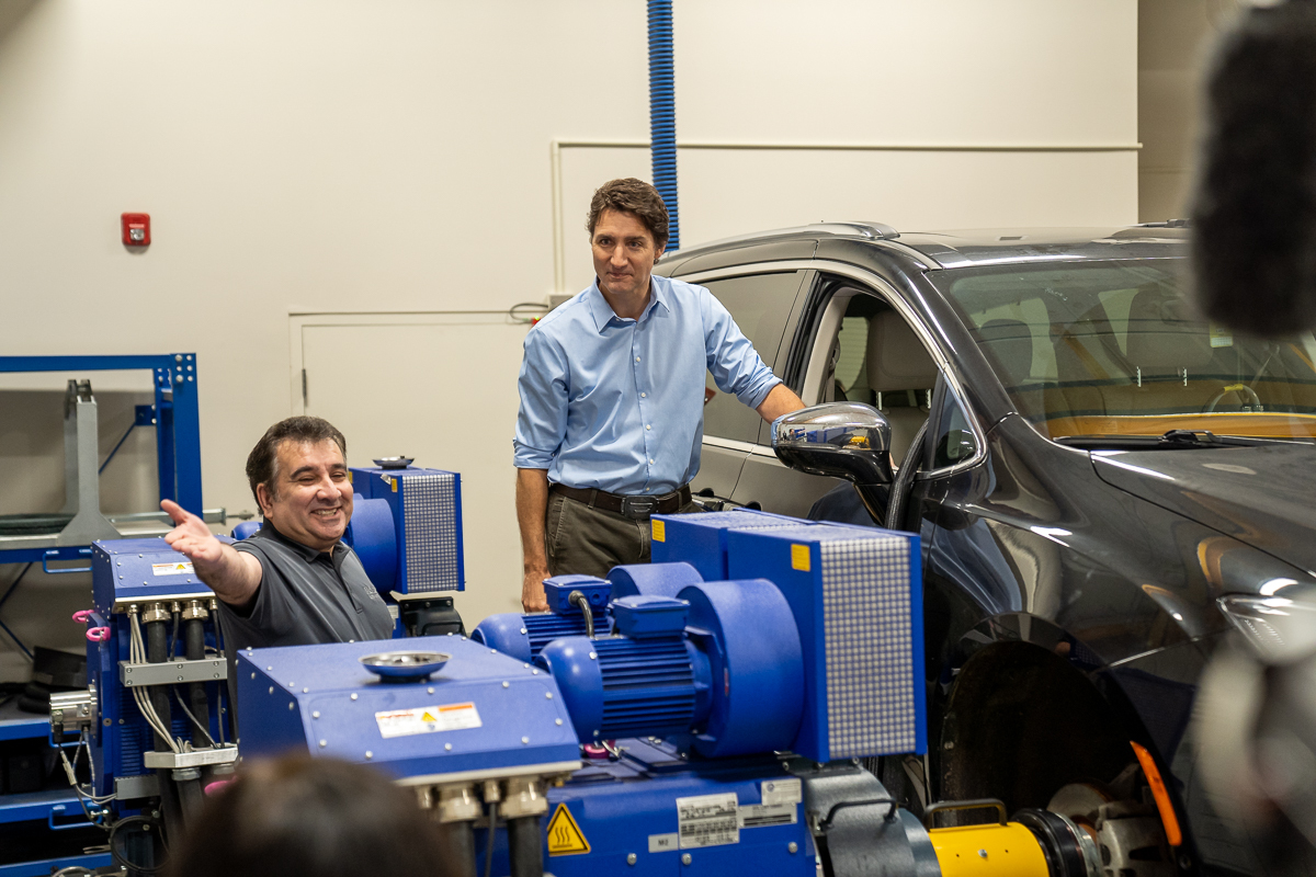 The PM leans against a vehicle on a platform as Canada Excellence Research Chair and engineering professor Ali Emadi gestures out of frame at his postdoctoral fellow. 