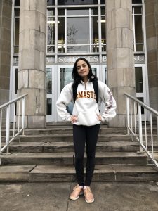 A woman wearing a white McMaster sweatshirt standing in front of a stone building