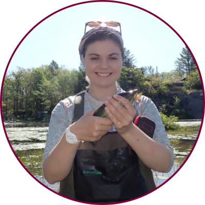 McMaster student Danielle Montocchio stands in a wetland holding a fish in her hands. 