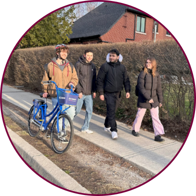 Four students walk to McMaster campus. One student pushes a bike. 